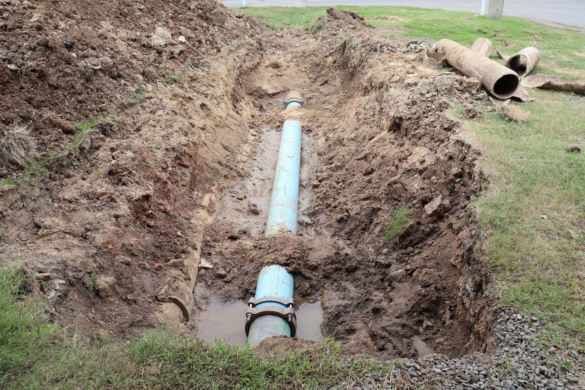 Trench with blue PVC pipe being installed in a dirt excavation, with grass on either side.