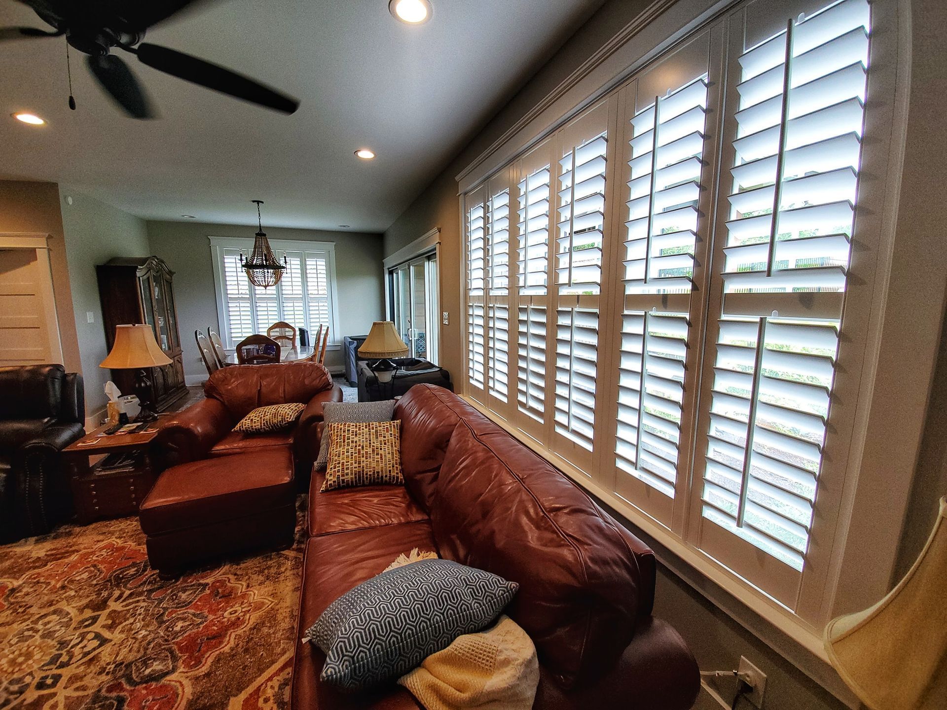 Living room with leather sofa, patterned rug, white shutters, and chandelier.