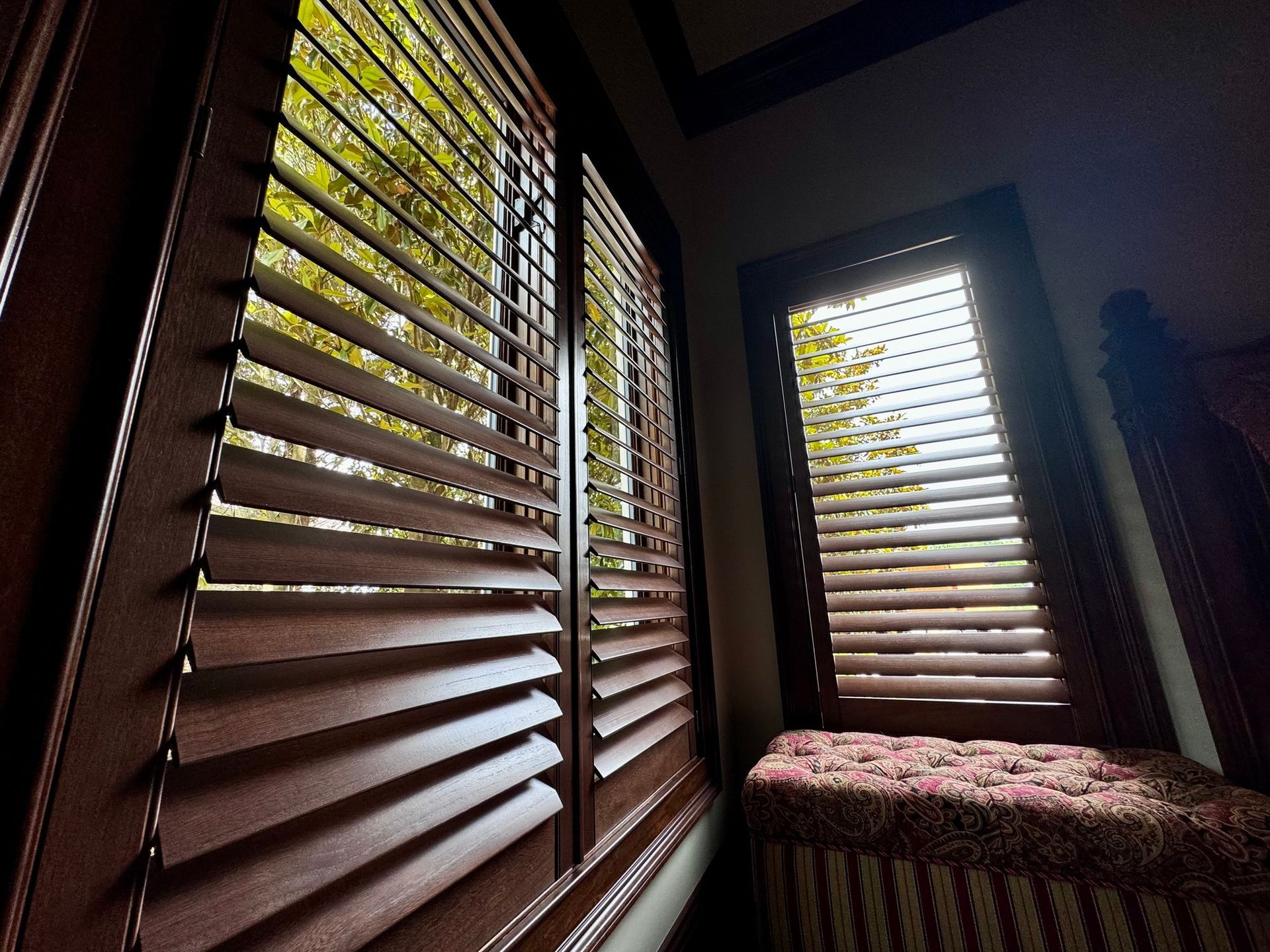 Wooden shutters on windows with a window seat; light streams through the slats.