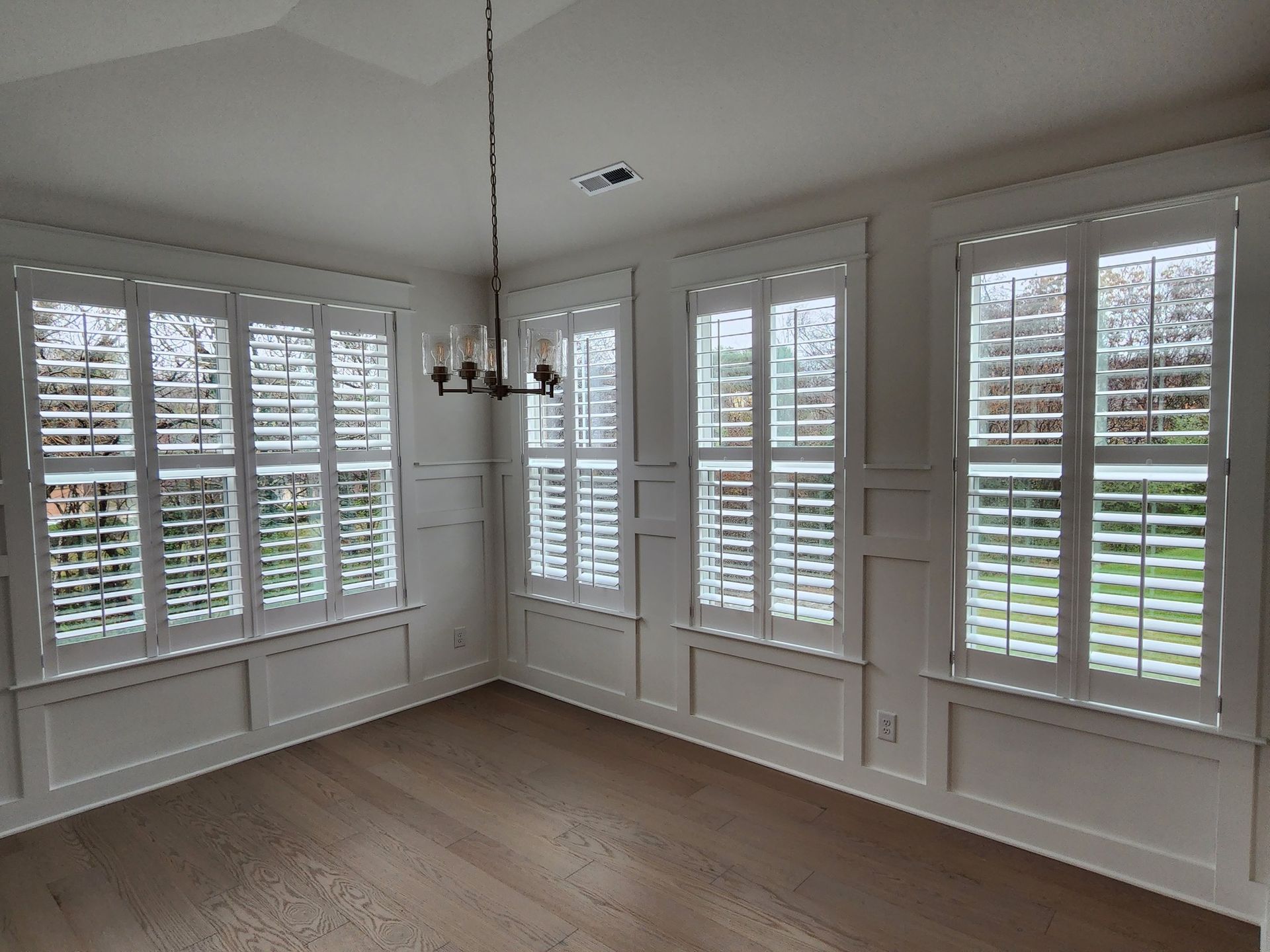 Empty dining room with white shutters, light hardwood floors, and a chandelier.
