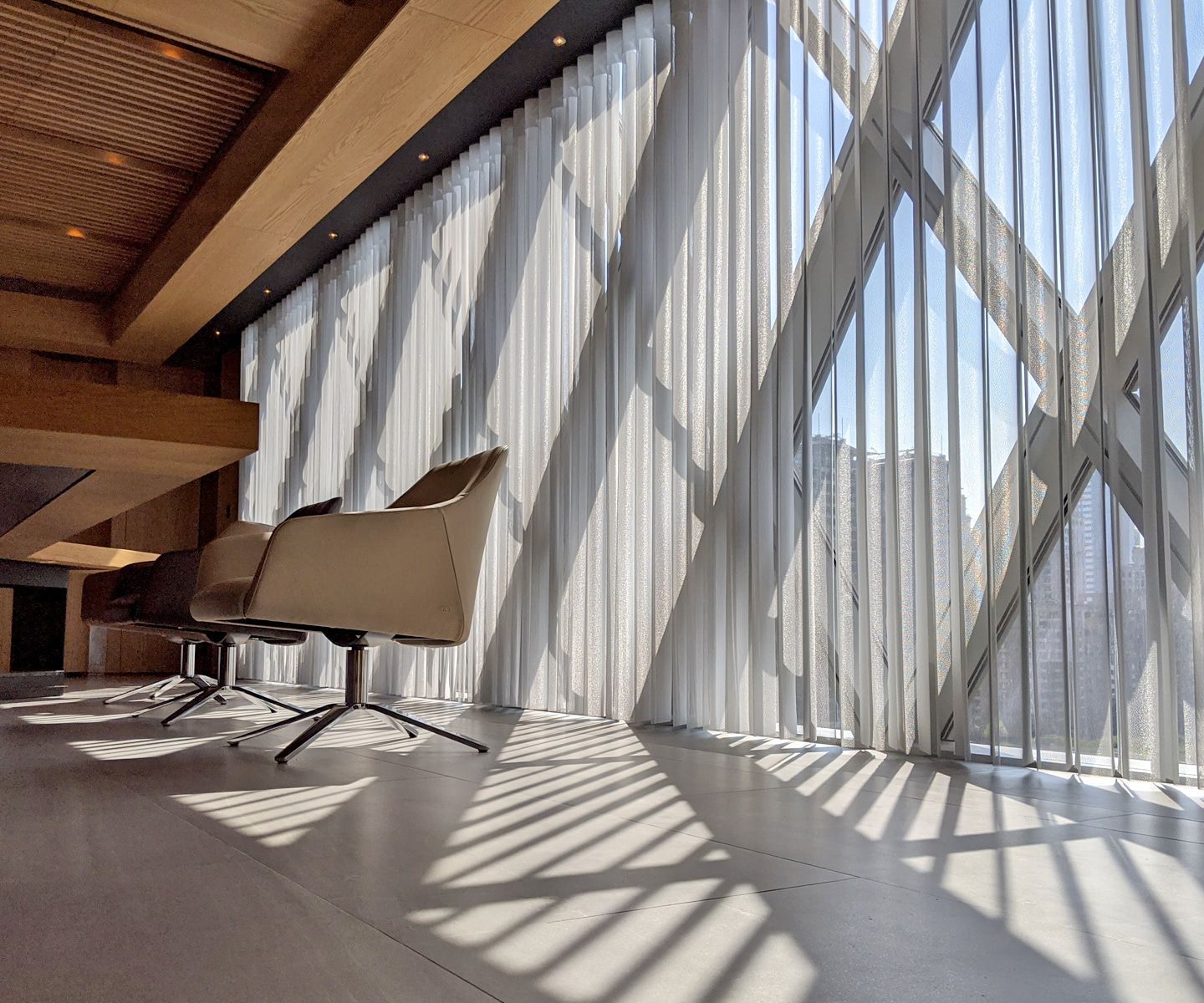 Modern interior with chairs by large window, casting striped shadows on the floor.