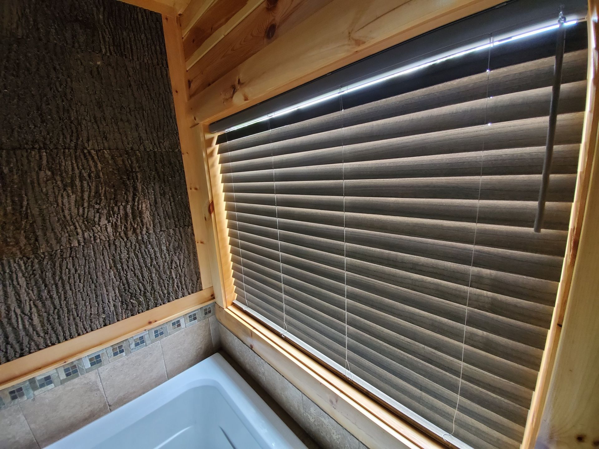 Bathroom window with closed brown blinds, wooden frame, and tree bark wall.