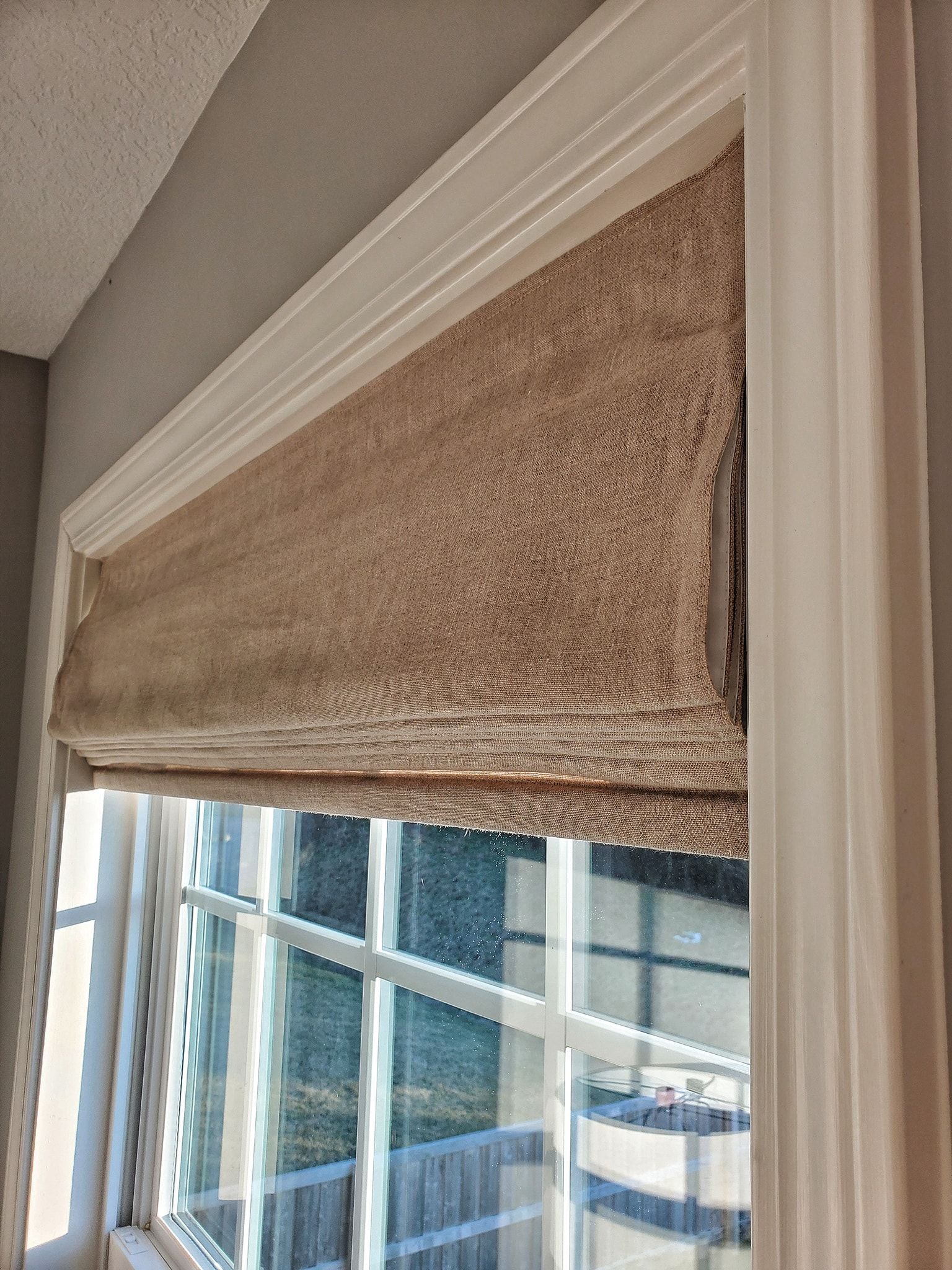 Tan Roman shade over a window with white trim, set indoors.
