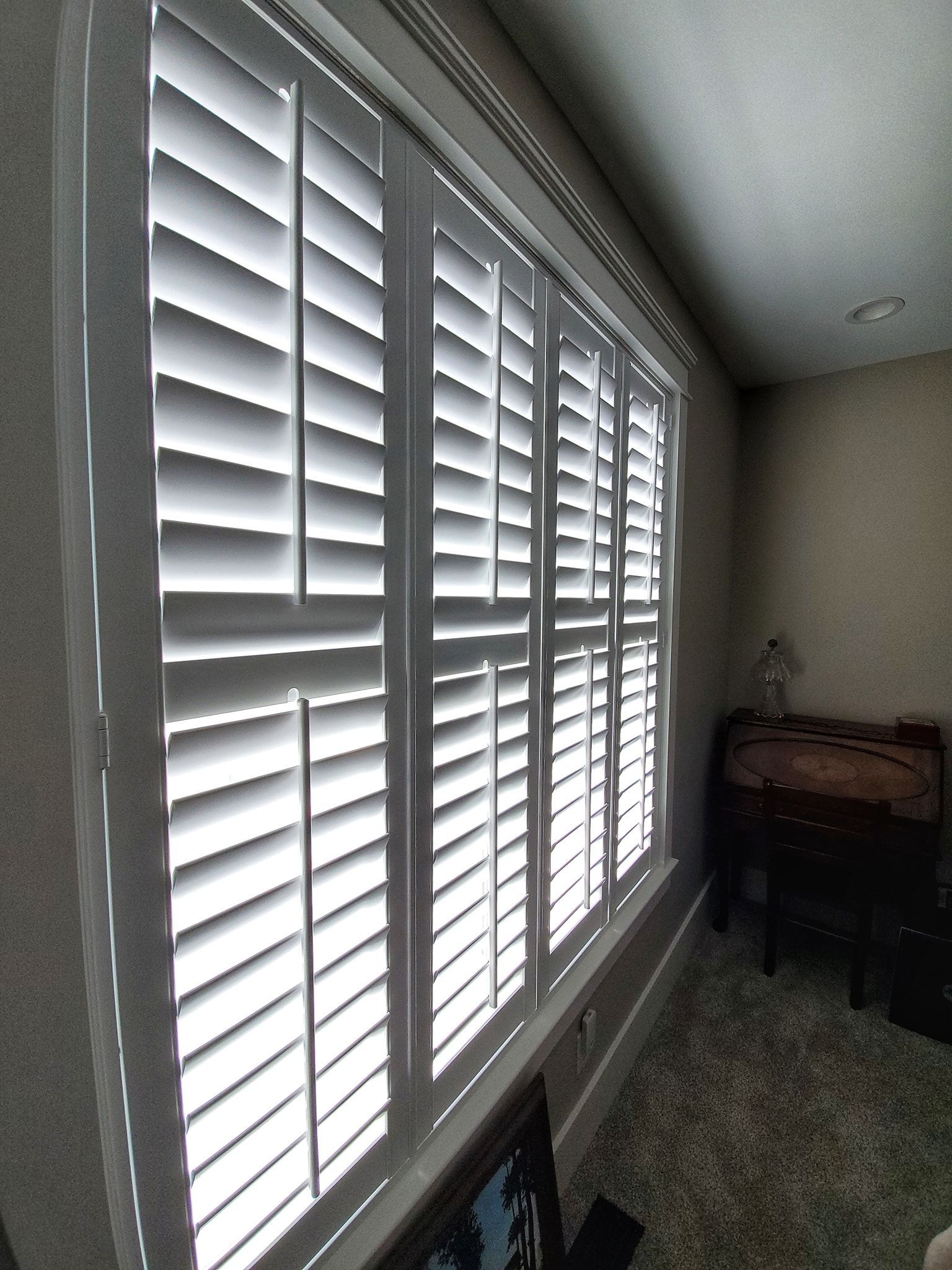 White window shutters with angled slats, allowing diffused light into a room.