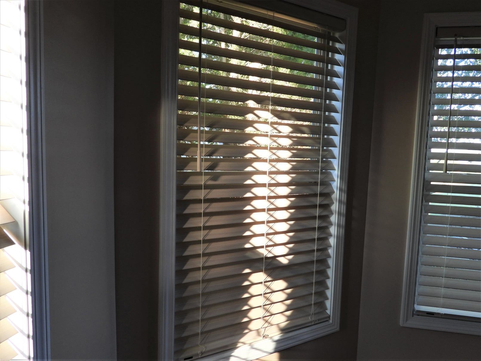 Window with closed blinds, sunlight streaming through, casting shadows on the wall.