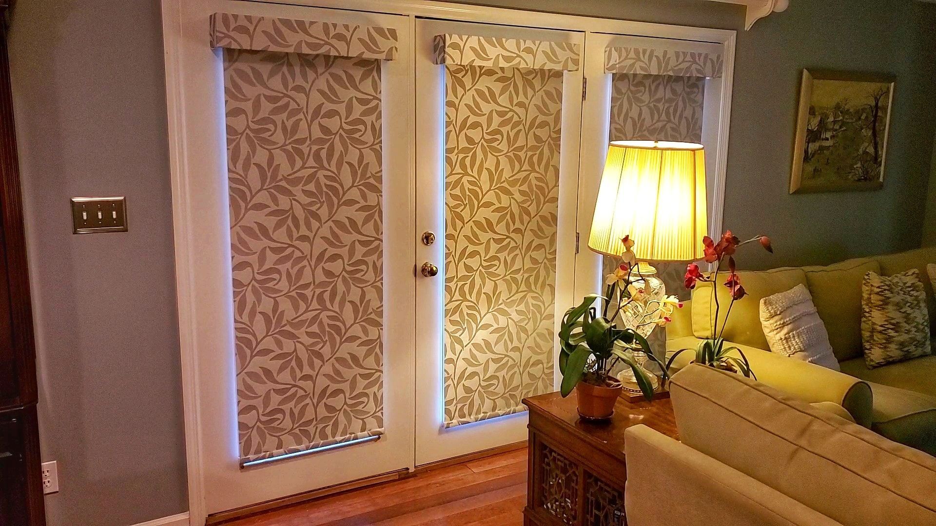 French doors with patterned shades, lit by a lamp and leading to a living room with a couch.