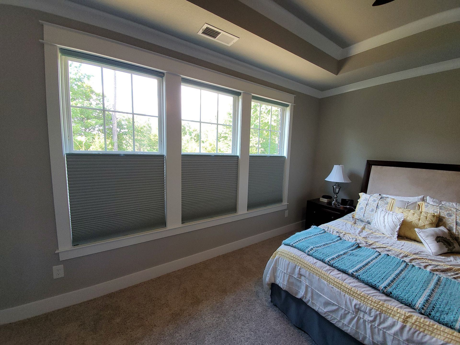 Bedroom with three windows, gray shades, beige carpet, and a bed with a blue blanket.