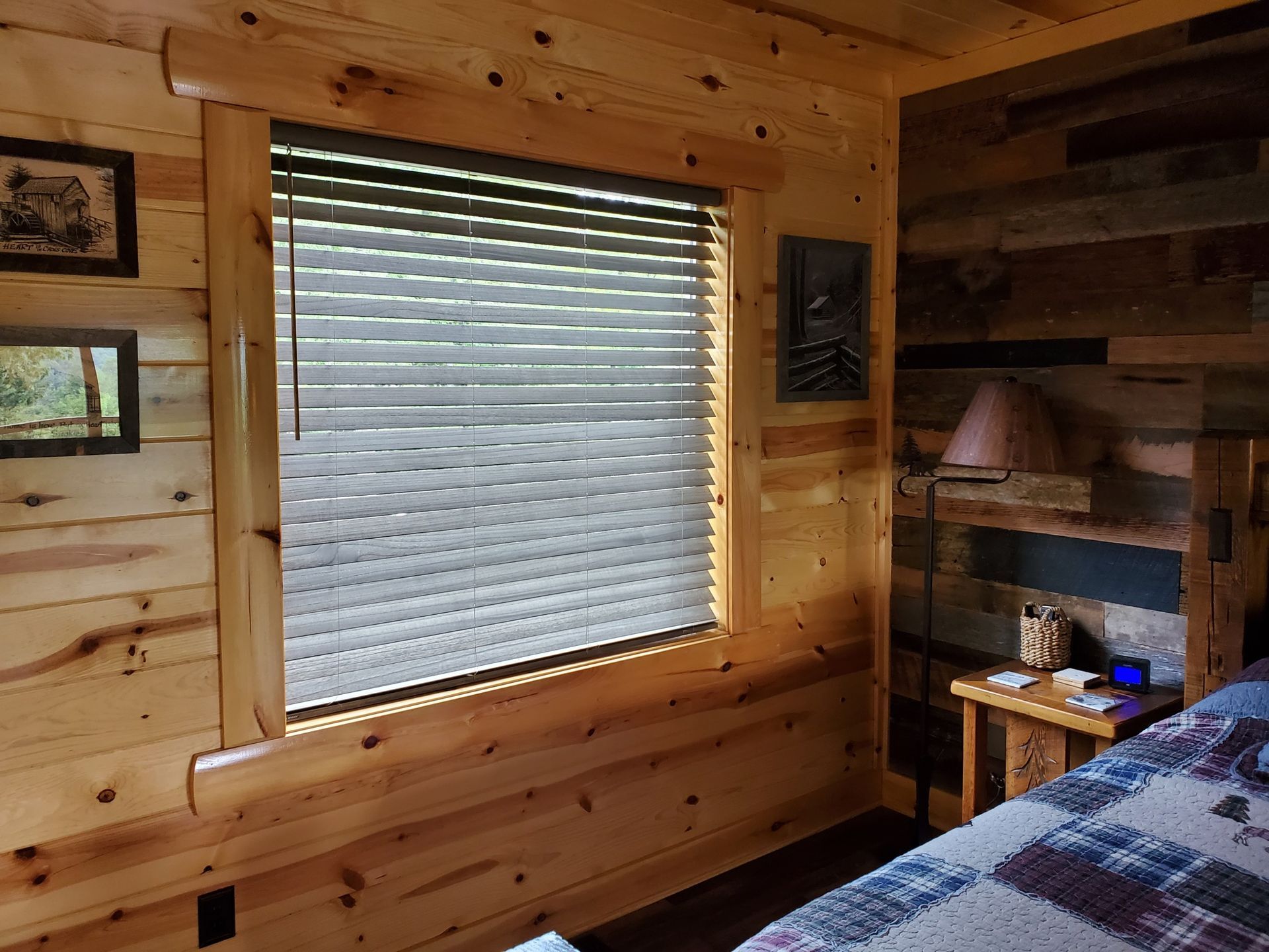 Log cabin interior with a window, wood blinds, and a bedside table.