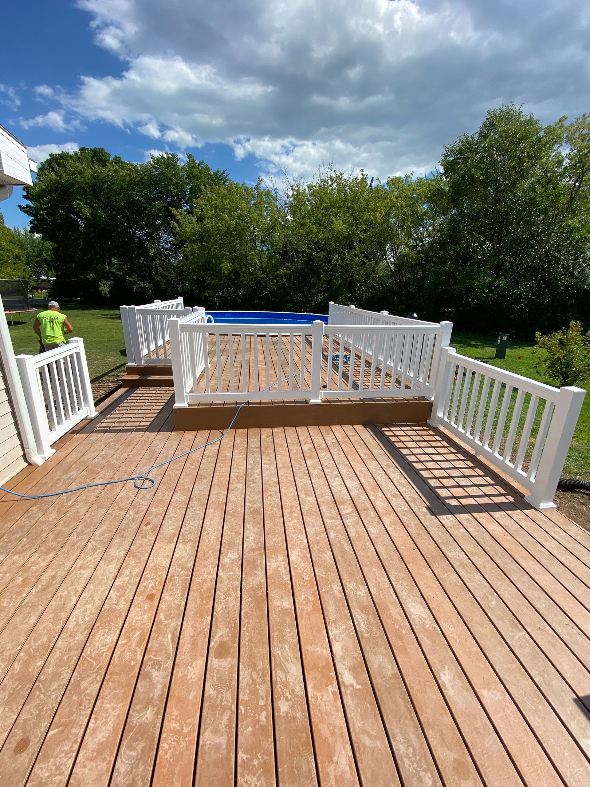 A wooden deck with a white railing and a pool in the background.