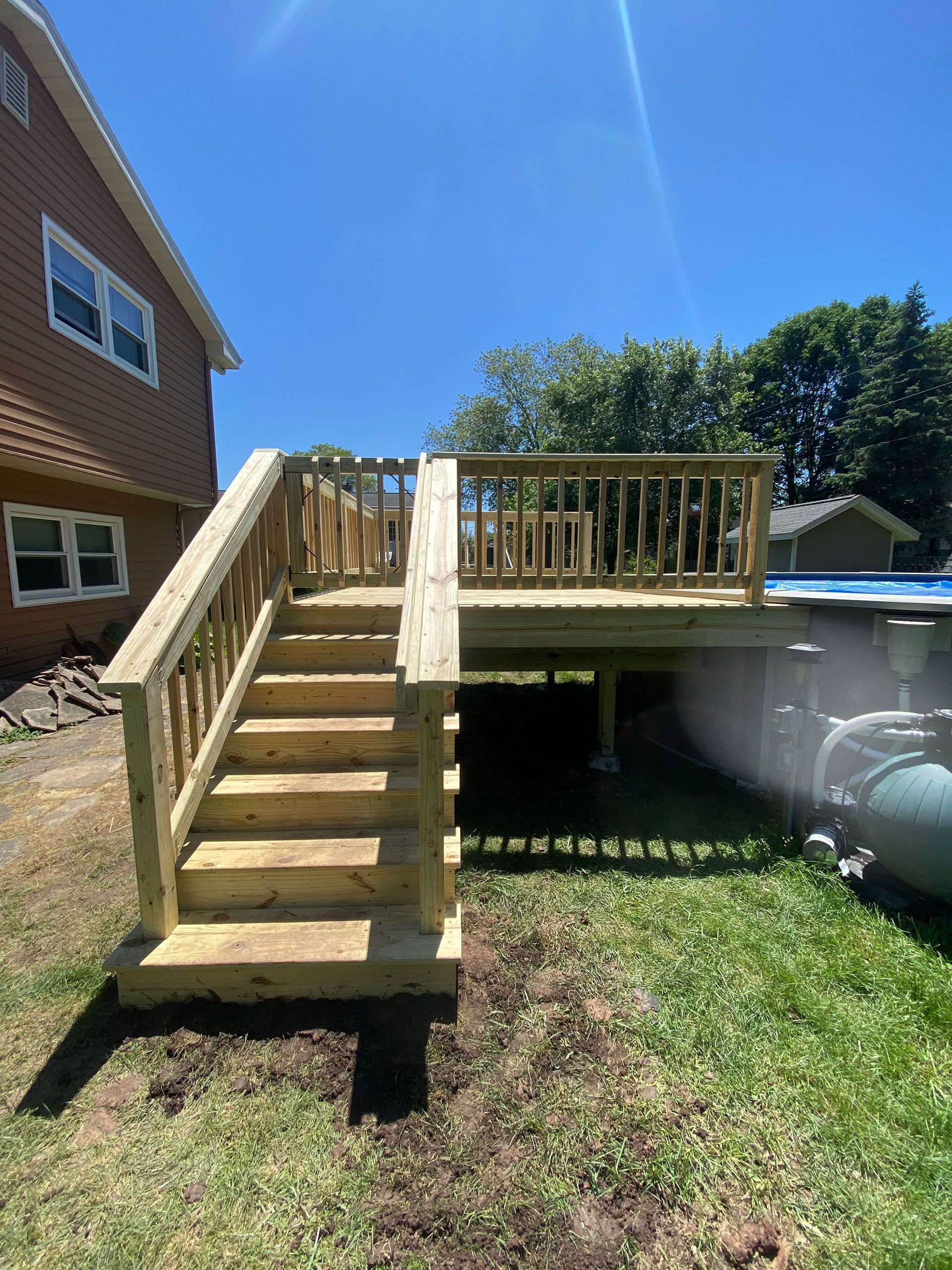 A wooden deck with stairs leading up to it is in the backyard of a house.