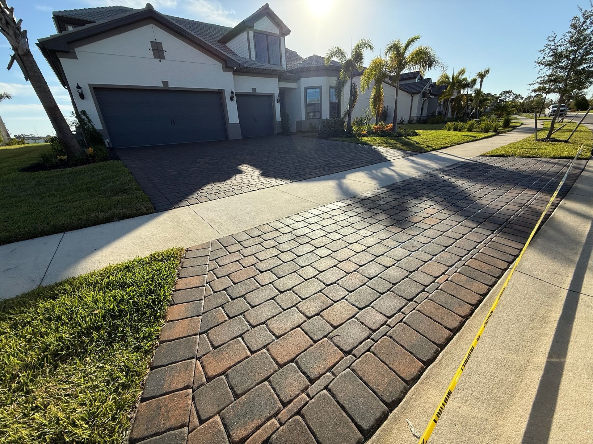 Two-story white house with black driveway, green lawn, and blue sky.