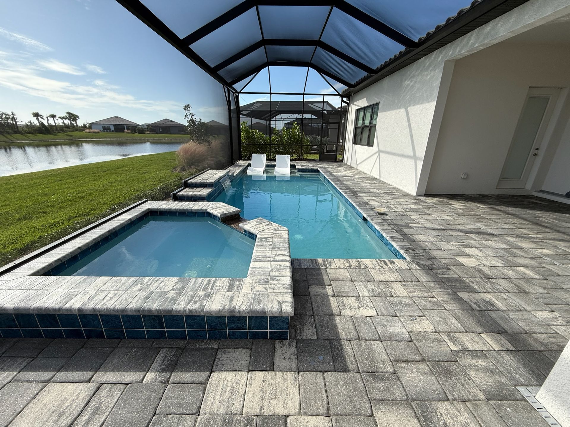 Stone path curves alongside a blue swimming pool, with green bushes on one side.