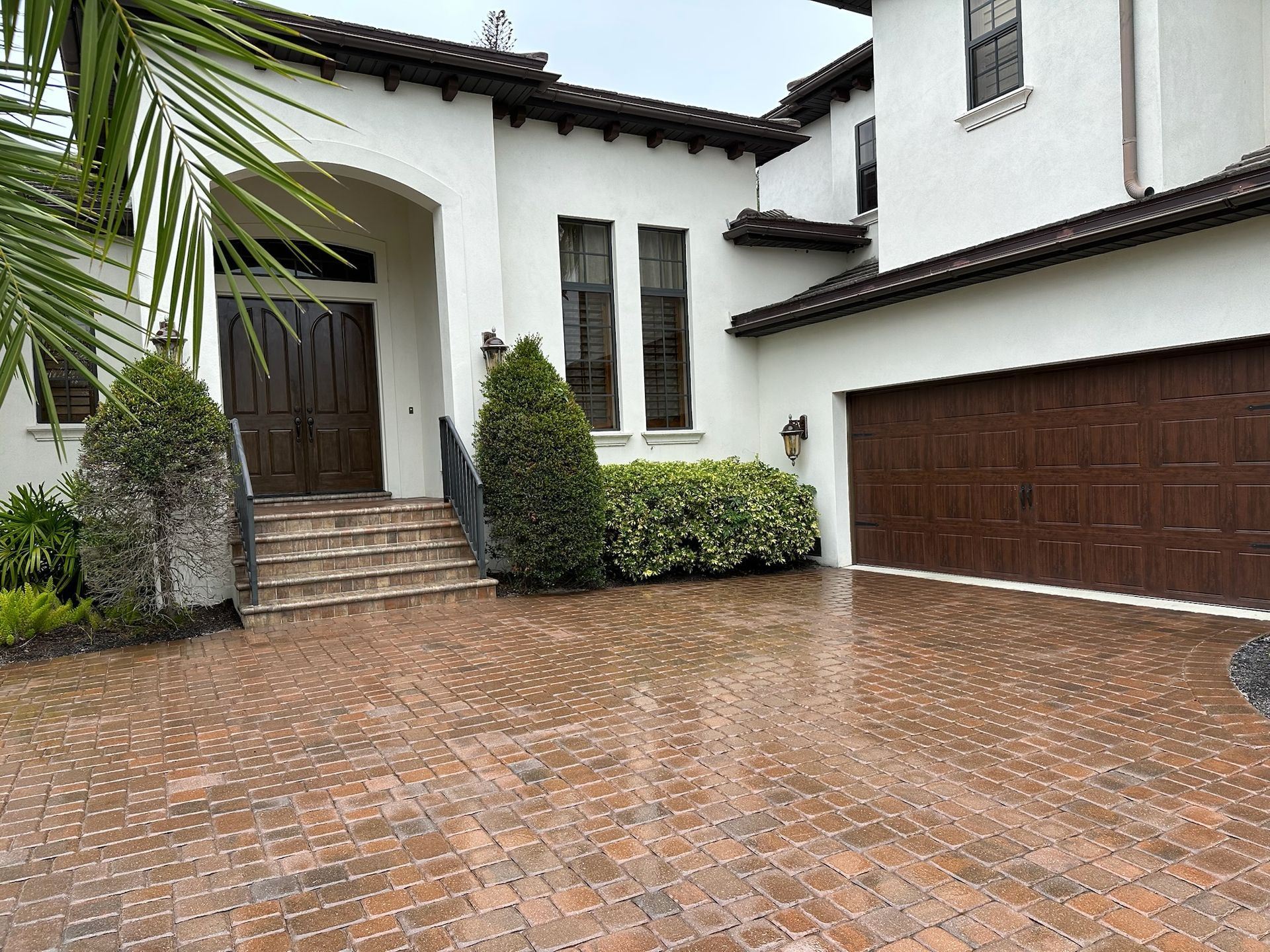 Curved, stamped-concrete pathway with a brick pattern, bordered by greenery and grass, lit by sunlight.