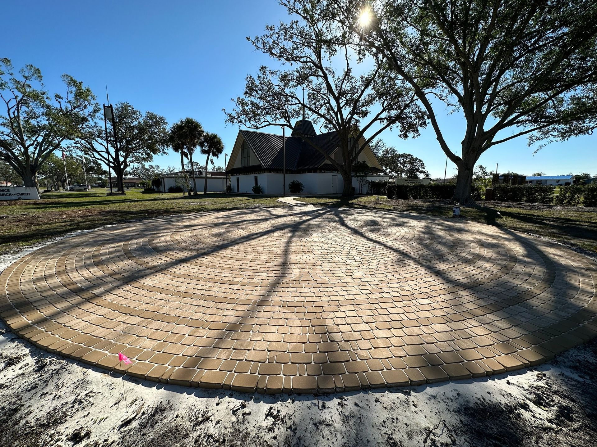 Hands wearing work gloves placing a brick paver on a gravel surface, with a mallet visible.