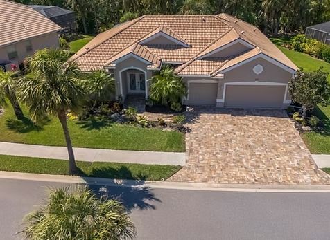 Tan stucco house with a tile roof, palm trees, and a stone driveway.