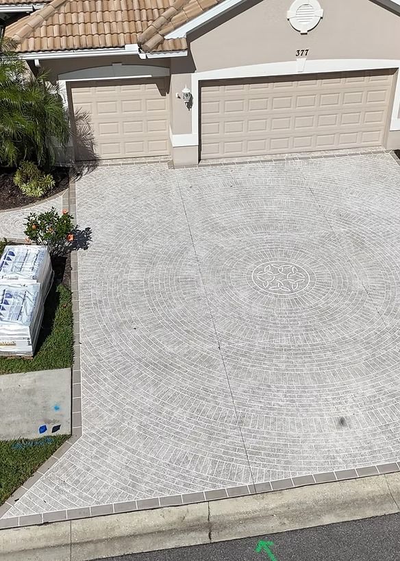 Driveway paved with light gray bricks, leading to a house with beige garage doors.