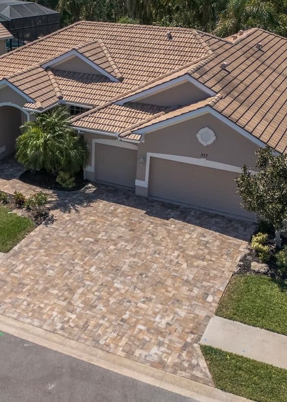 Beige house with a tiled roof and a brick driveway.