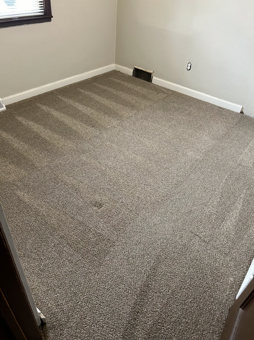 Empty room with brown speckled carpet, beige walls, and a small vent.