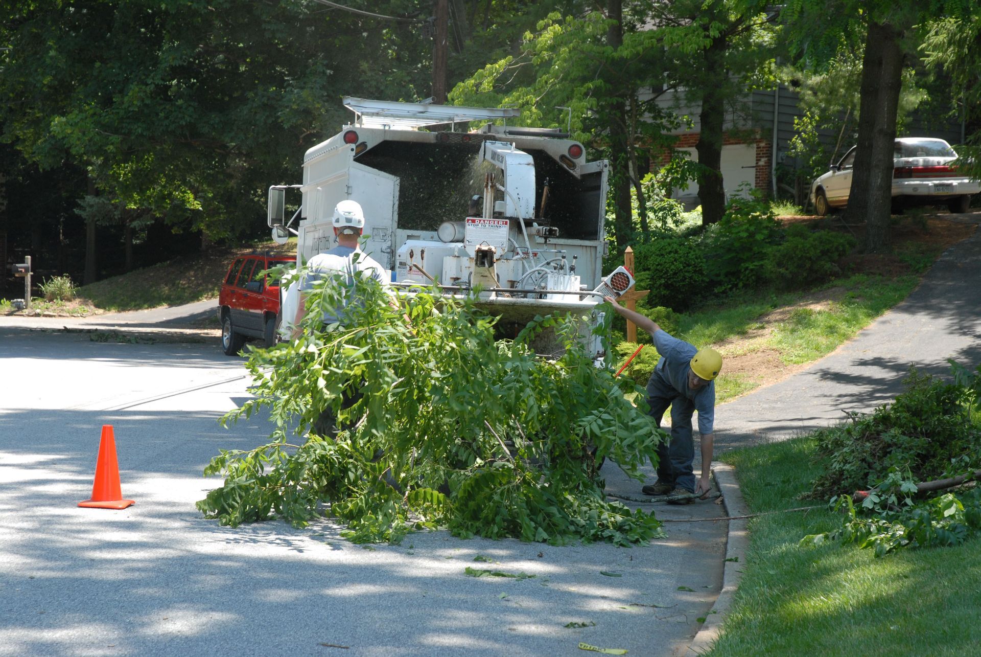 Two workers in hard hats feed tree branches into a wood chipper parked on a residential road.