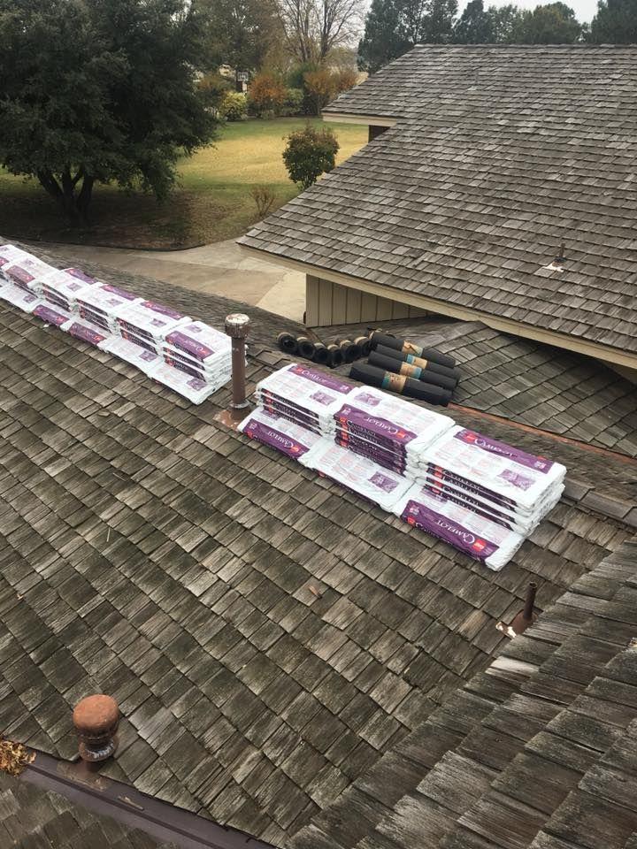 Rooftop with bundles of new shingles and rolls of underlayment, ready for installation.