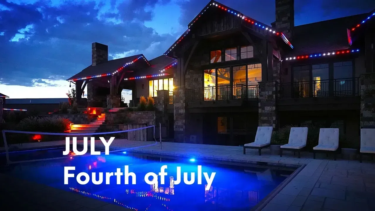 Luxurious house illuminated with red, white, and blue lights for Fourth of July, poolside.