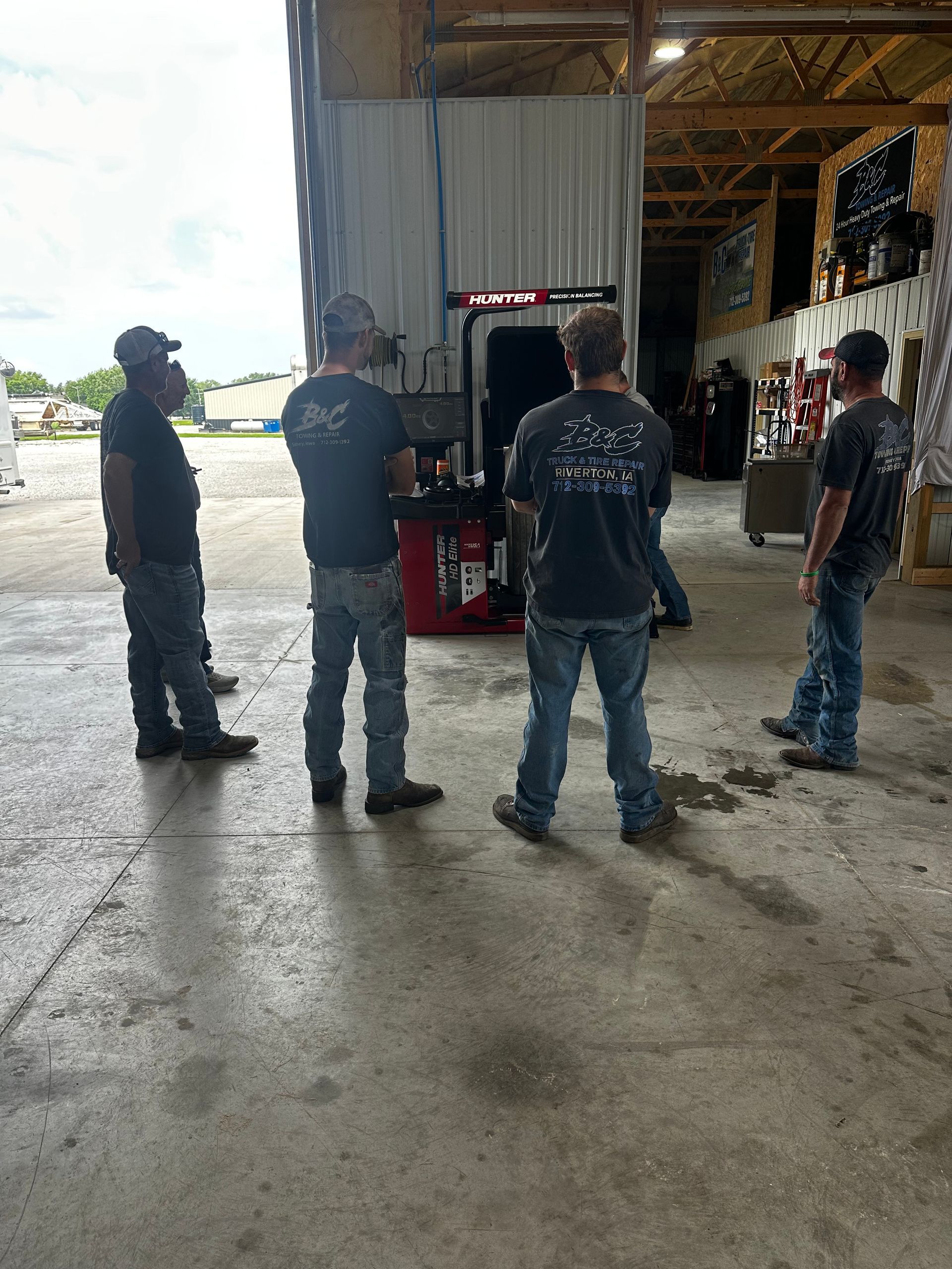 Workers standing in a warehouse near a red forklift, seen from behind on a wet concrete floor.