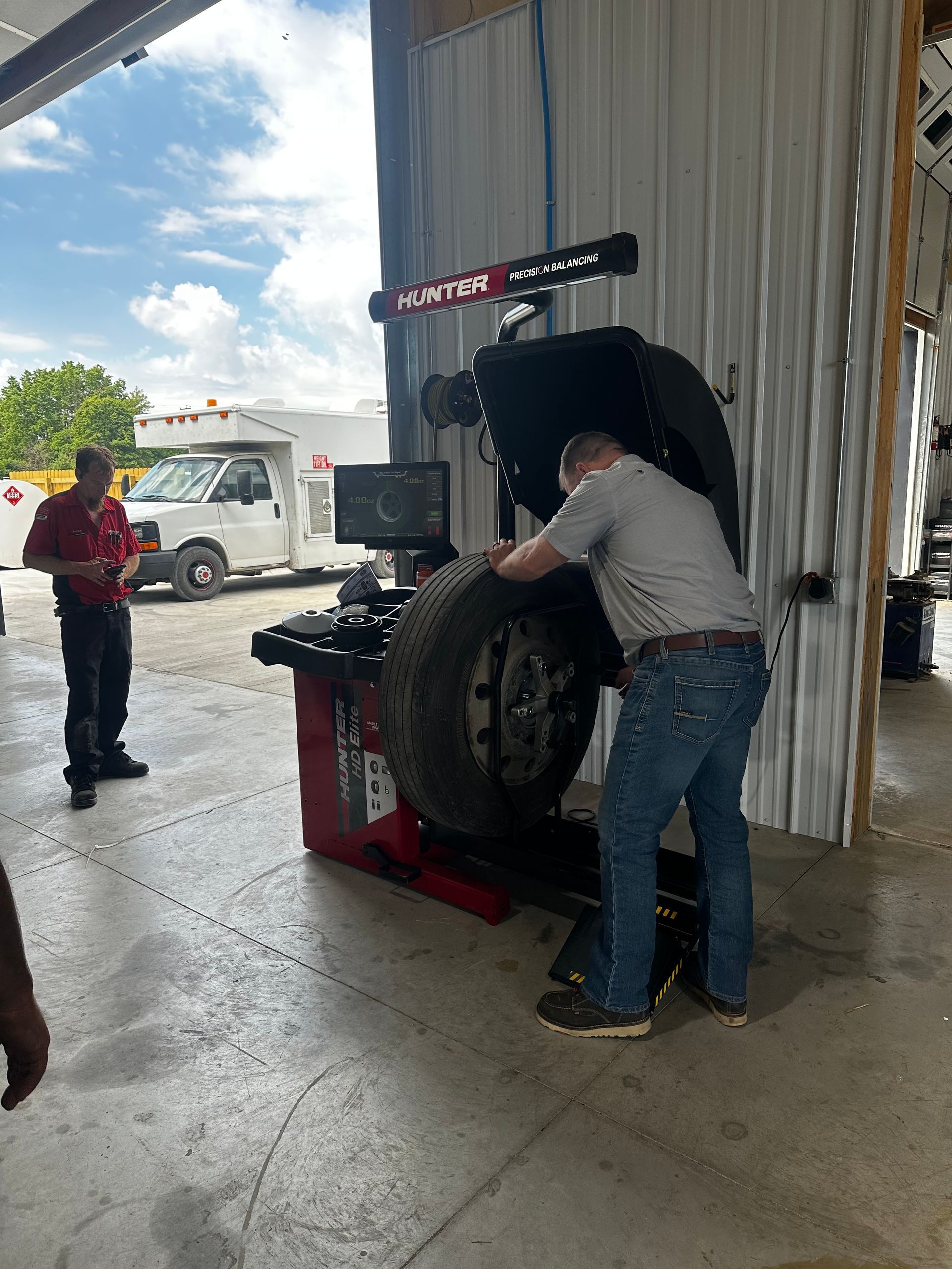 Two people servicing a tire on a red wheel balancer in a garage workshop