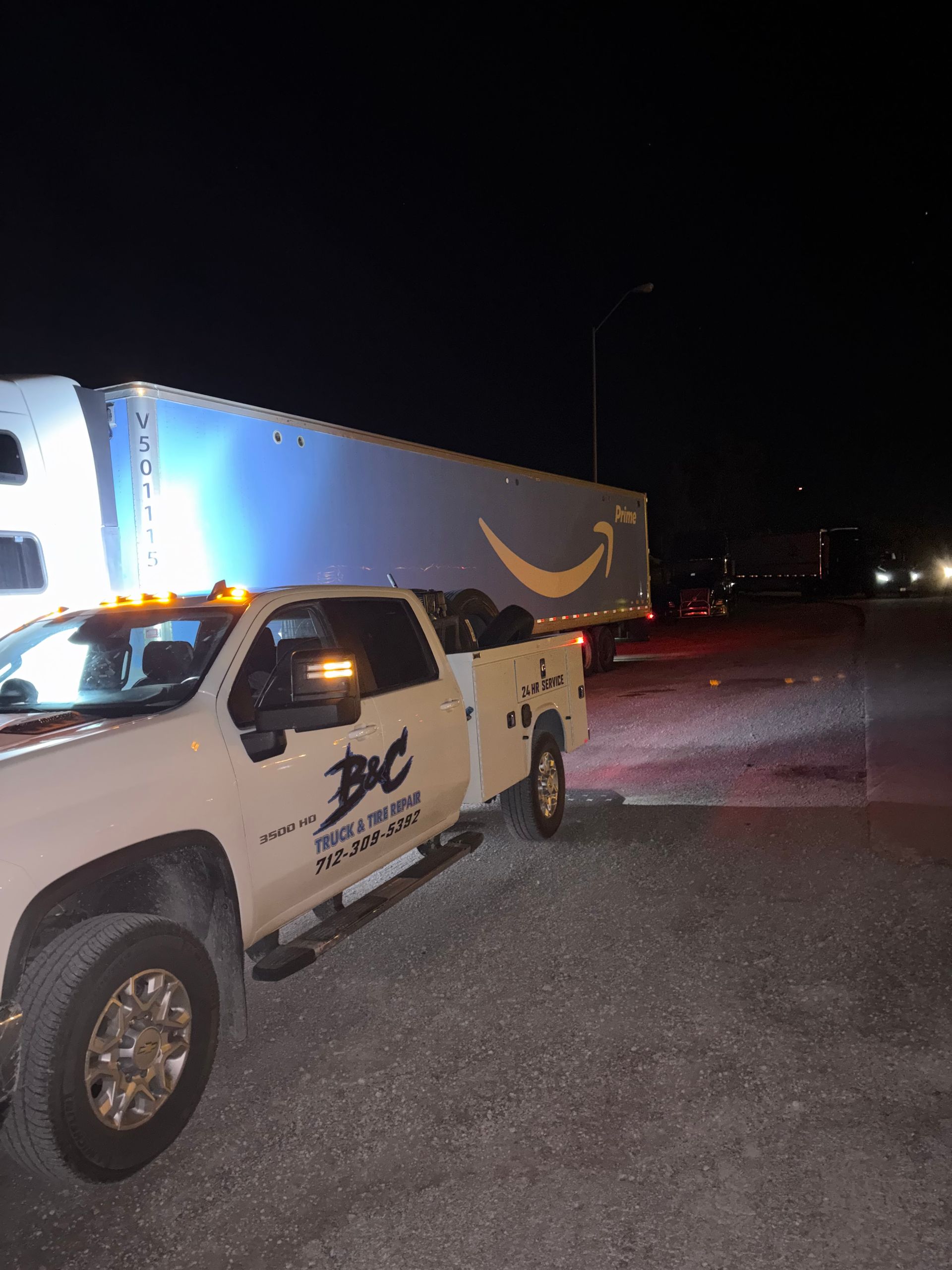 White pickup truck parked beside a semi-trailer at night in a dimly lit lot