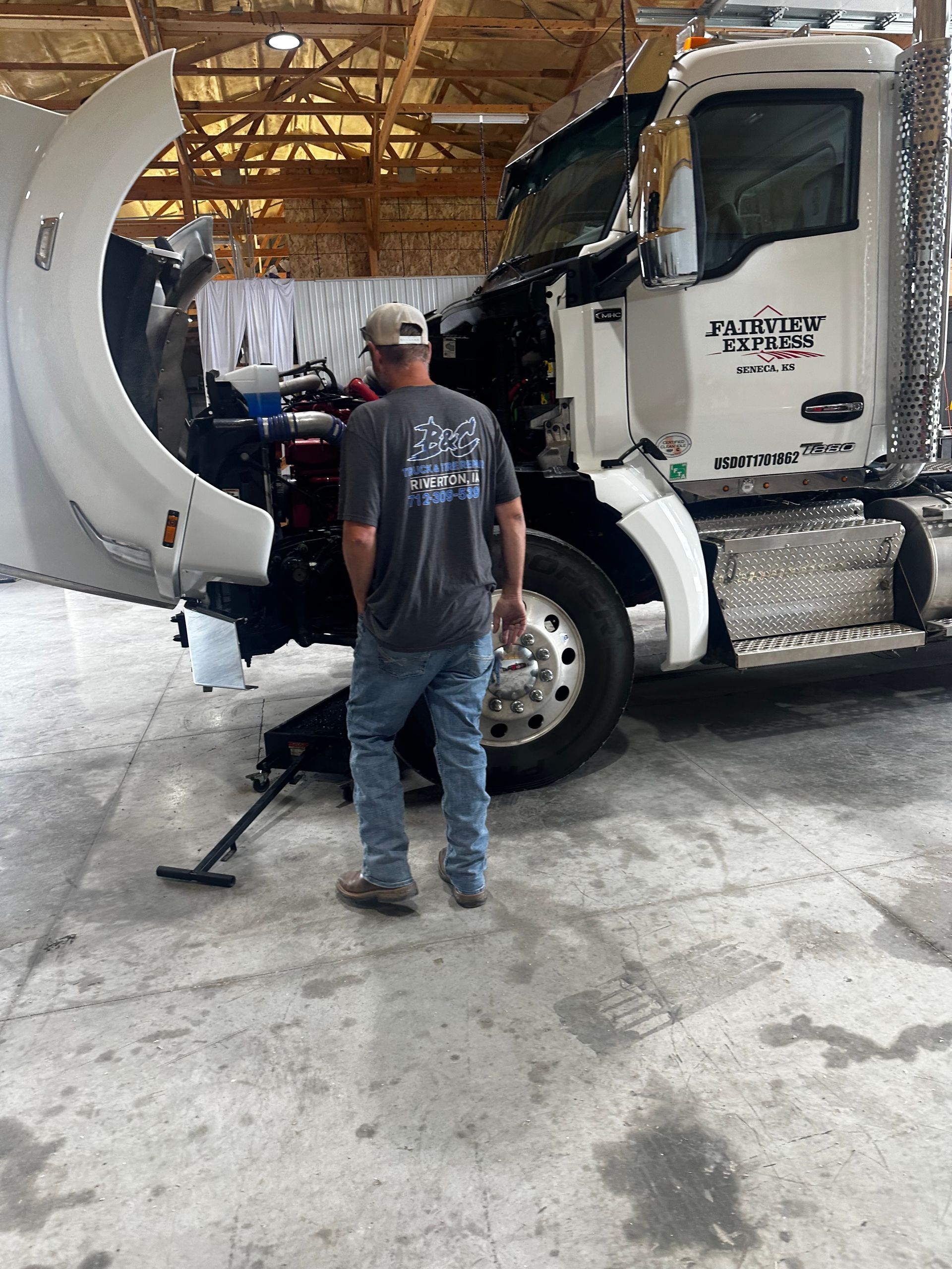 Mechanic inspecting a white semi-truck in a warehouse garage with the hood open