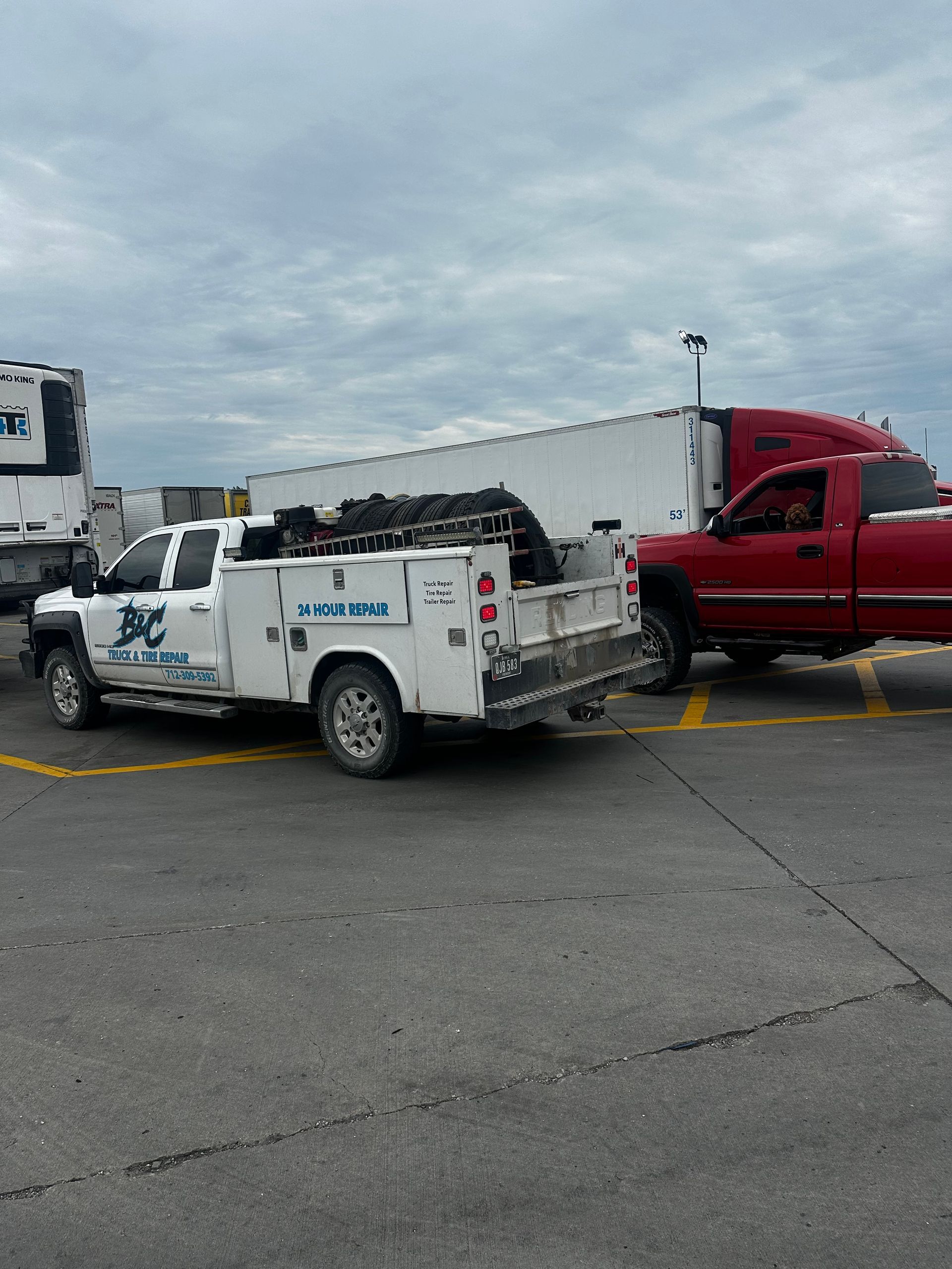 White utility truck and red pickup stopped close together in a parking lot under cloudy skies