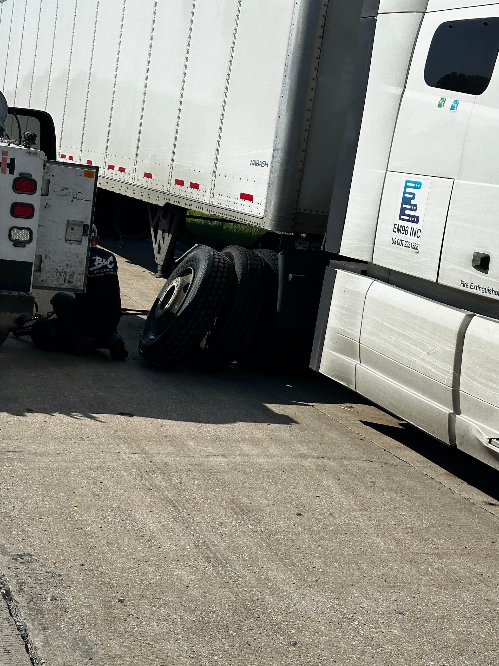 White semi-truck cab and trailer jackknifed in a roadway, with debris or damaged wheel beneath the trailer.