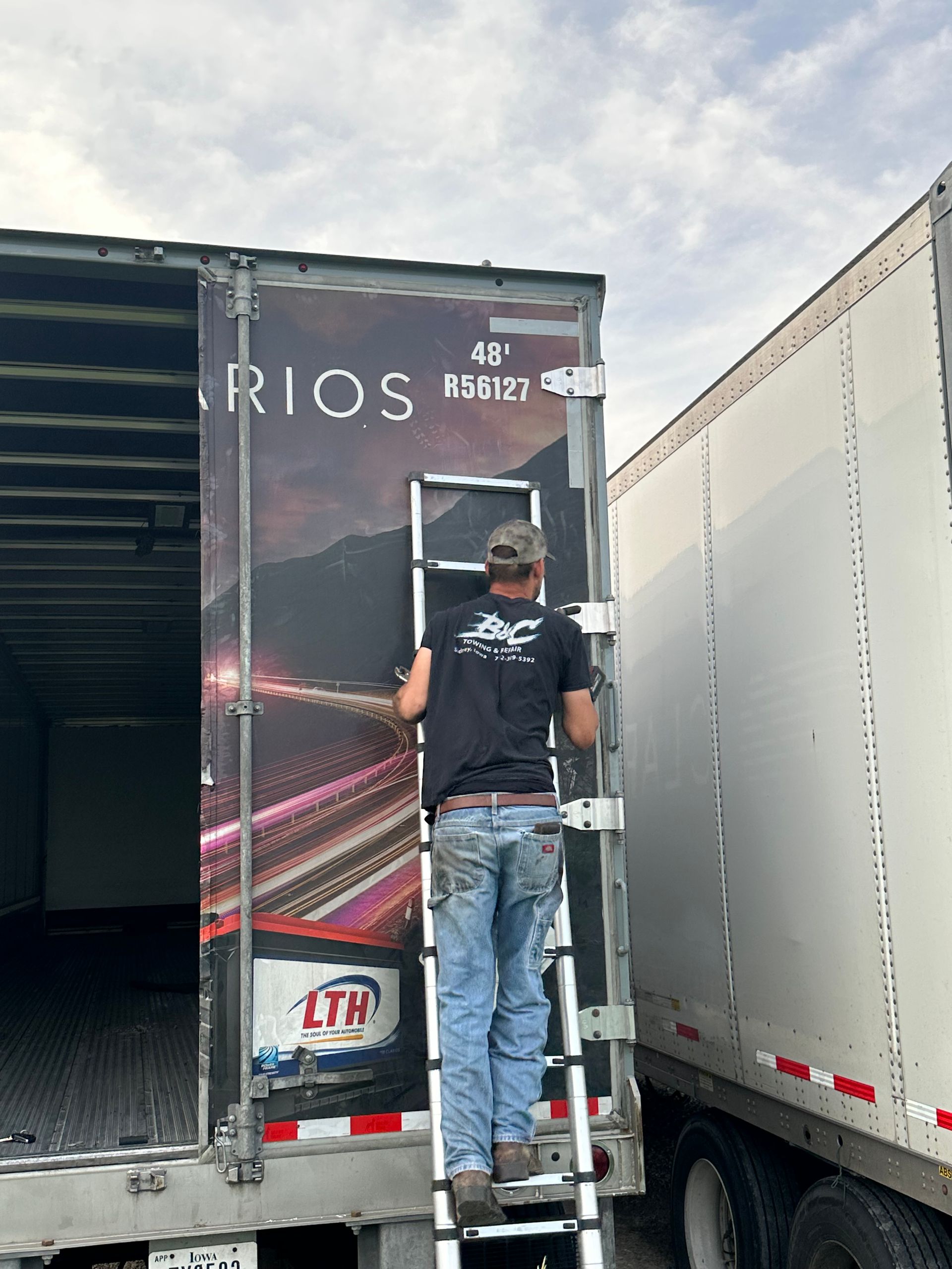 Person standing on truck steps beside a large trailer, reaching toward the back door.