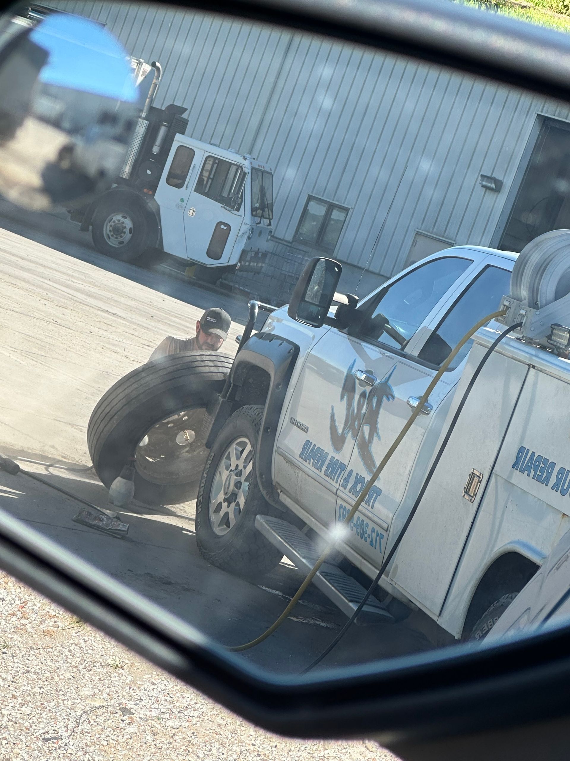 Tow truck and service pickup parked outside an industrial building, viewed through a car window.