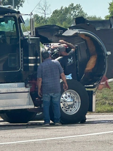 Tow truck driver inspecting a damaged black tanker truck on the roadside