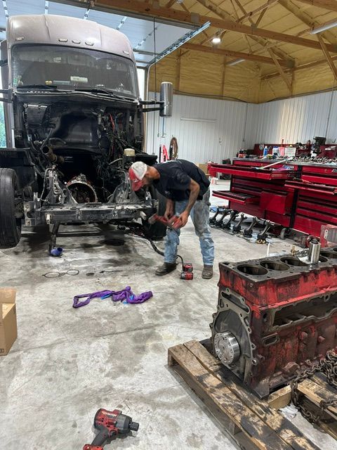 Mechanic inspecting a semi-truck engine in a workshop with tools and parts on the floor