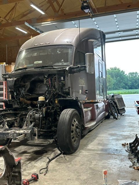 Truck cab under repair in a garage, front body removed and exposed engine visible.