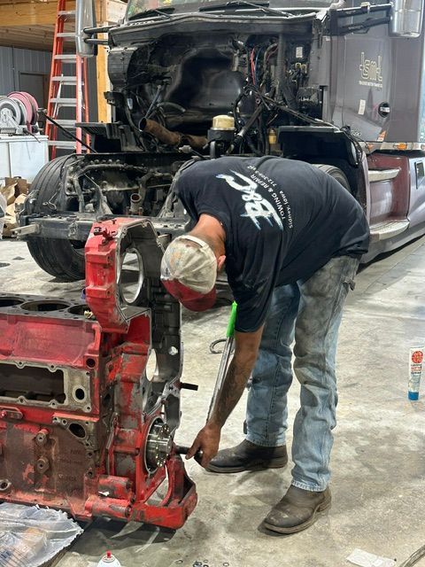 Mechanic working on a red engine block in a garage, with a truck cab in the background