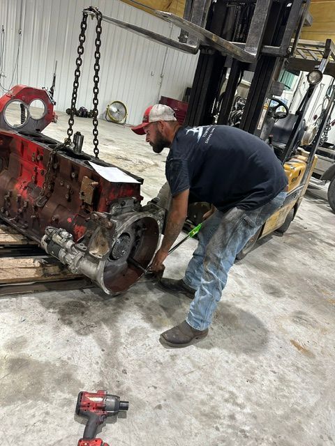 Mechanic working on a red engine block in a shop, with tools on the floor.
