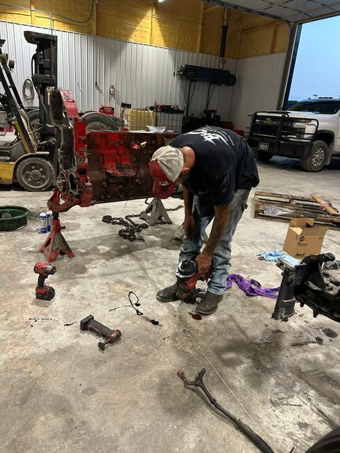 Mechanic working on a red tractor in a workshop, tools and parts scattered on the floor.