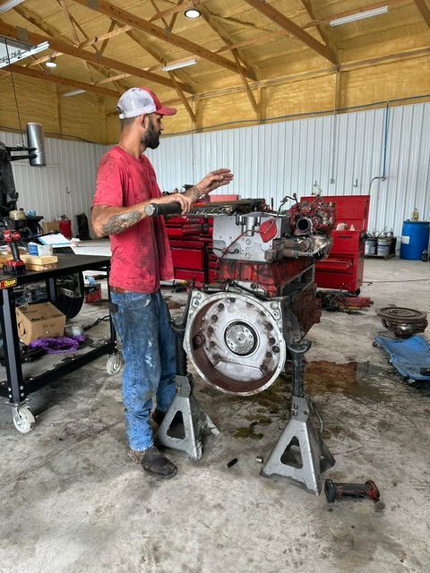 Mechanic standing beside a red engine block on stands in a workshop, working with tools.