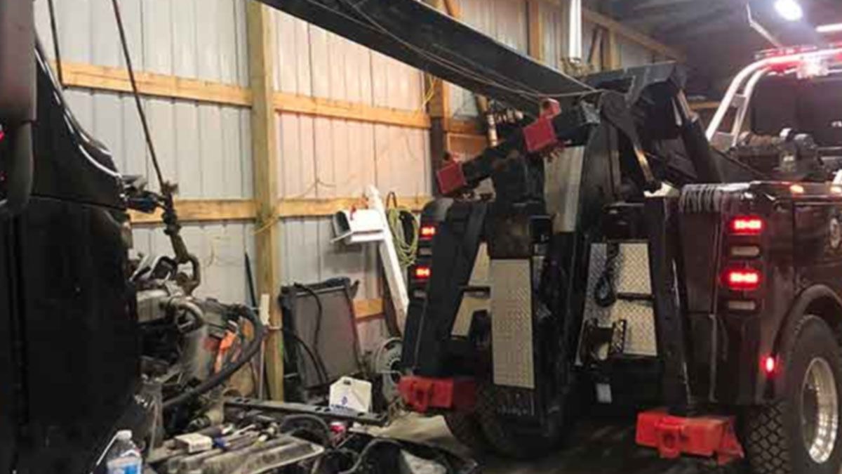 Tow truck with boom arm lifting equipment inside a garage workshop