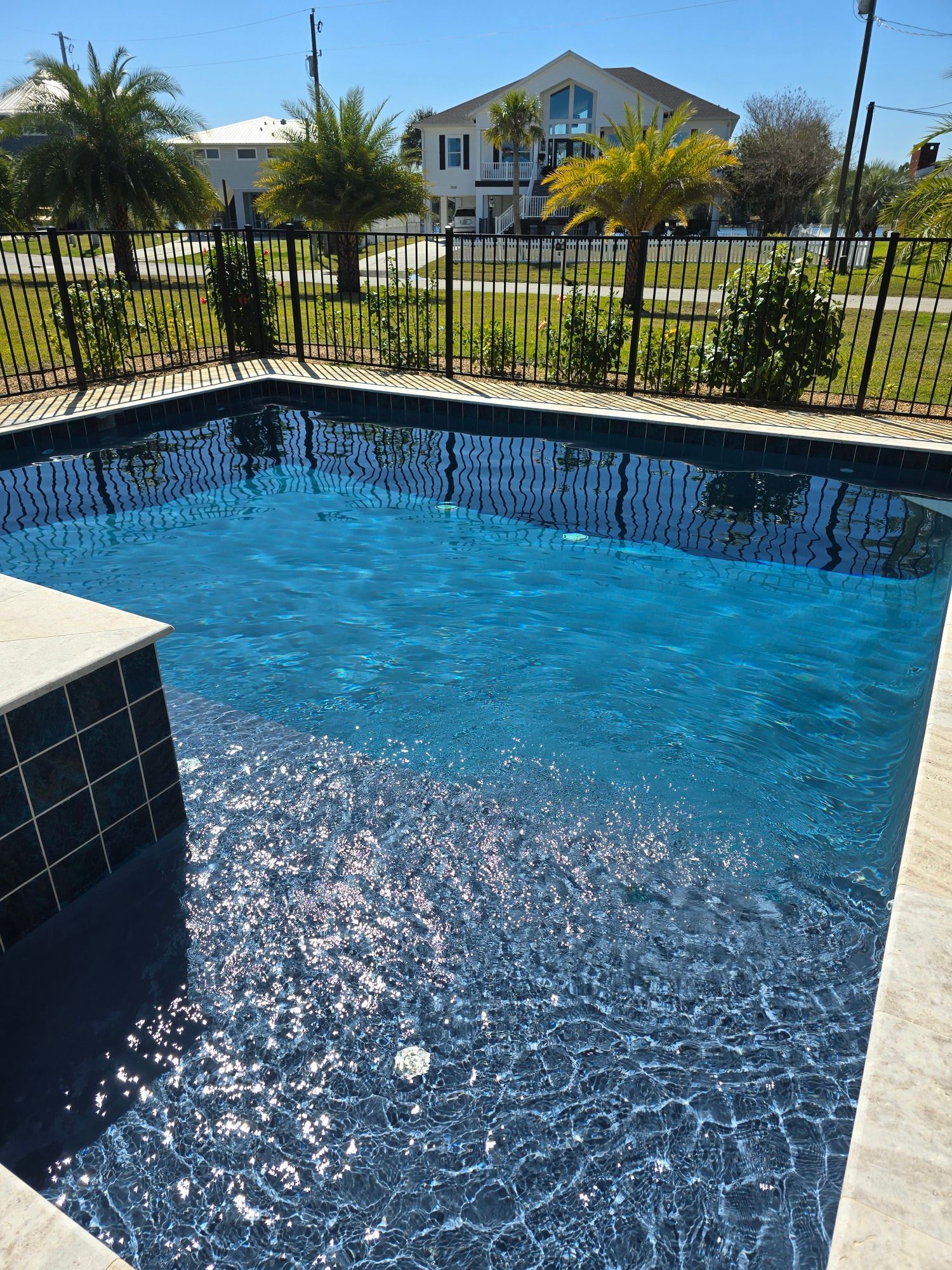 A large swimming pool with a fence around it and a house in the background.