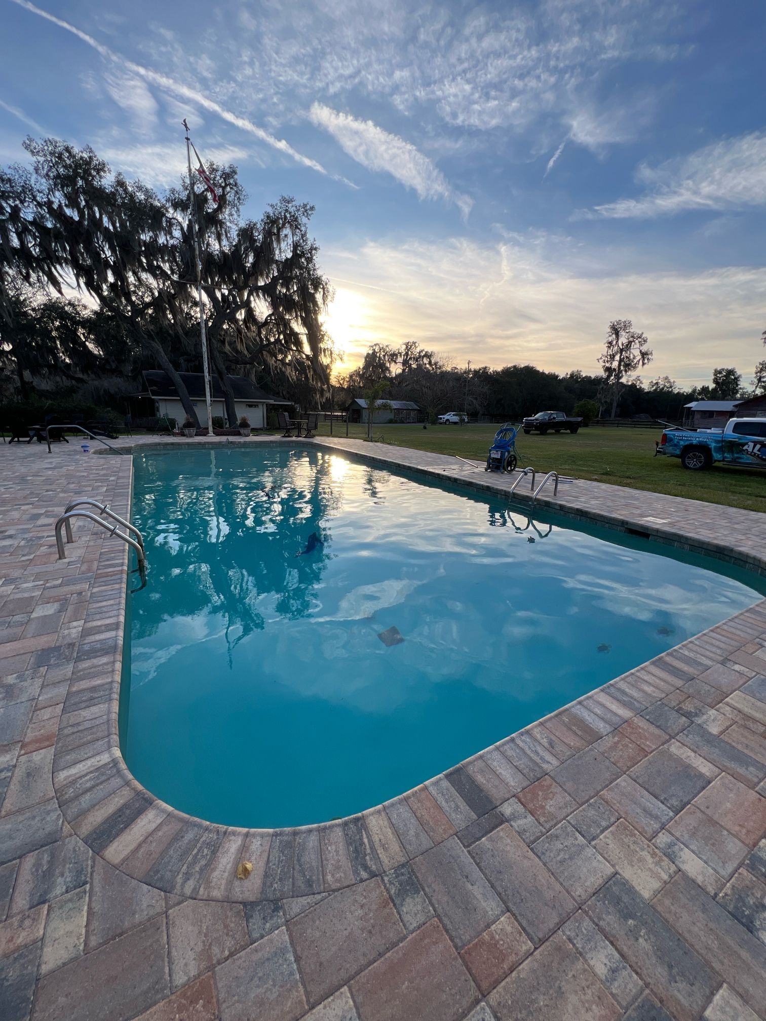 A large swimming pool with a brick patio and a sunset in the background.