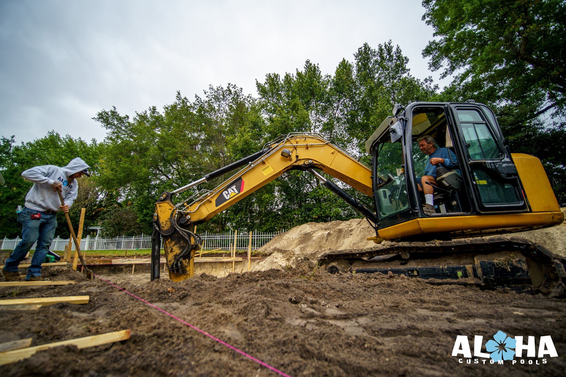 A man is driving a yellow excavator in a dirt field.