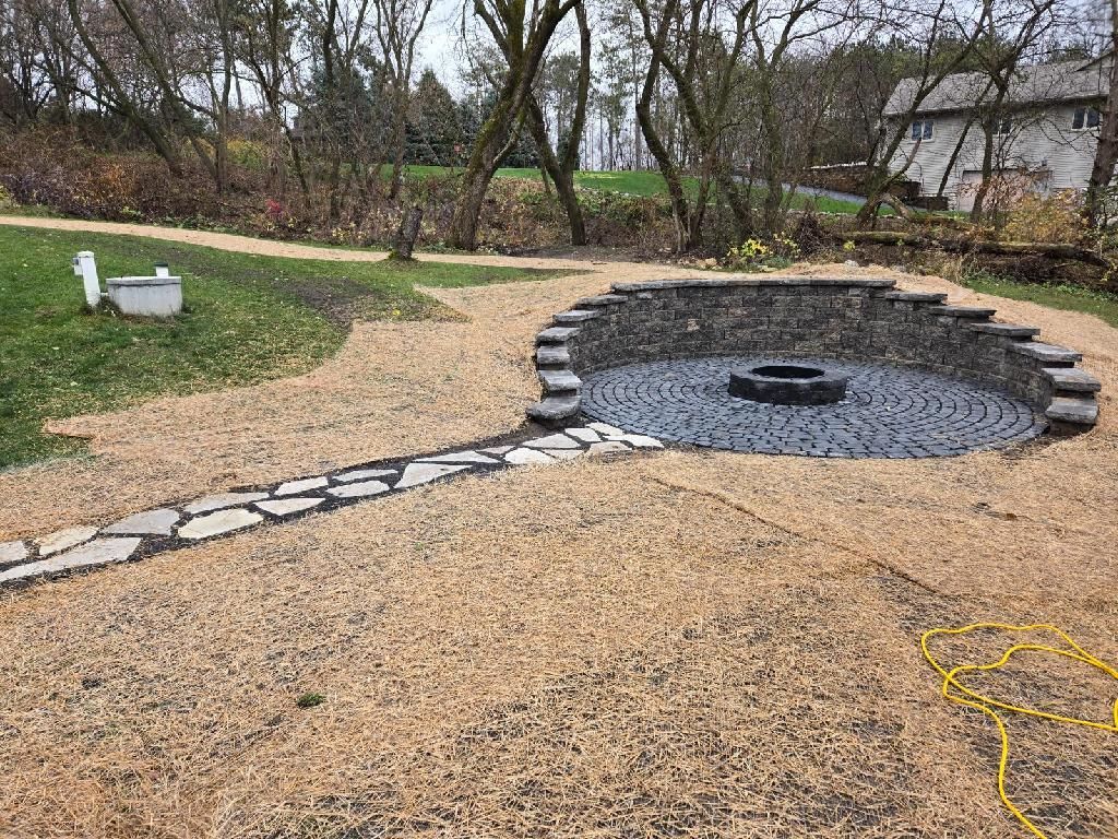 Stone fire pit with seating area, gravel ground, and stone path in a yard.
