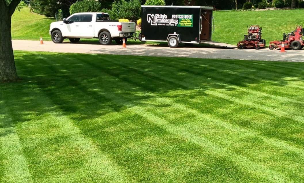 A white truck and trailer with lawn care equipment on a freshly mowed green lawn.
