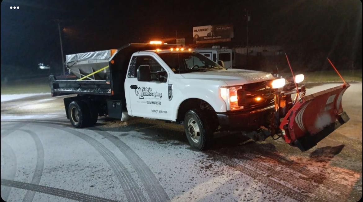 White snowplow truck clearing a snow-covered road at night with lights on.
