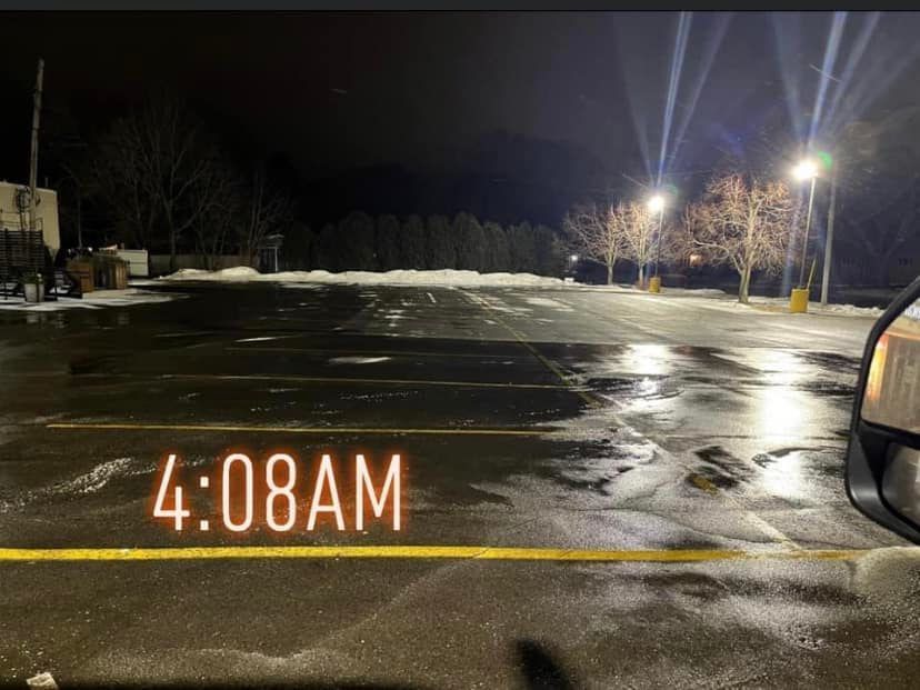 A dark parking lot at 4:08 AM, with snow, streetlights, and trees.