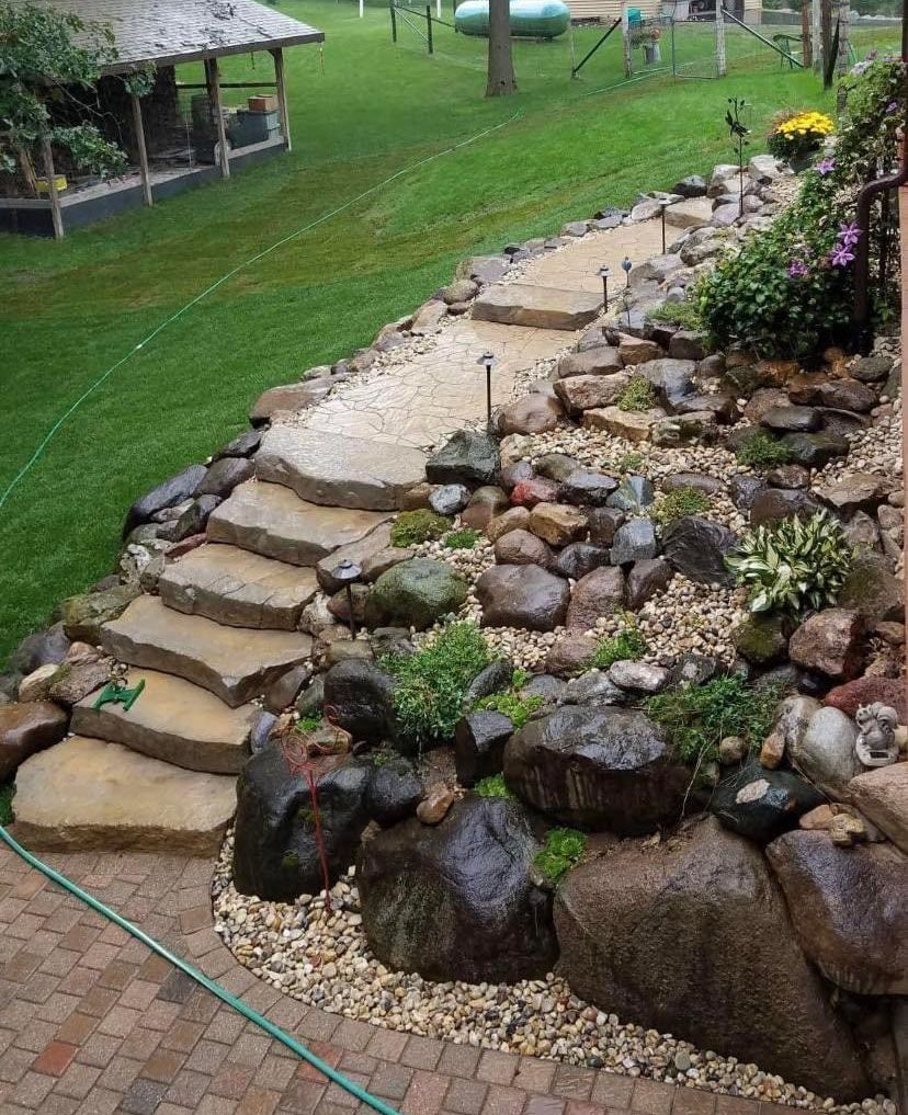 Stone steps and path winding up a grassy hill, flanked by rocks and plants.