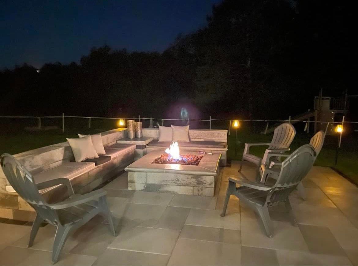 Nighttime outdoor seating area with lit fire pit, couches, and chairs.